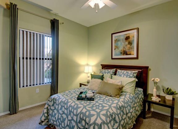 Cozy bedroom here at Pala Mesa Apartments with a bed featuring blue patterned bedding and multiple pillows. A bedside table with a lamp and decor creates a calm and inviting atmosphere.