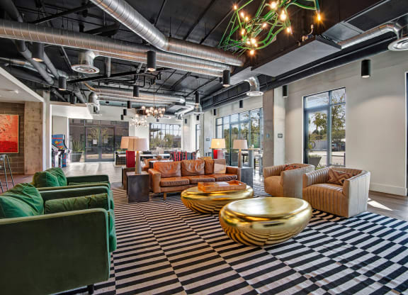 Modern lounge here at Roosevelt Row Apartments with striped carpet, leather and green velvet sofas, gold coffee tables, and exposed ductwork. Bright, airy, and stylish ambiance.