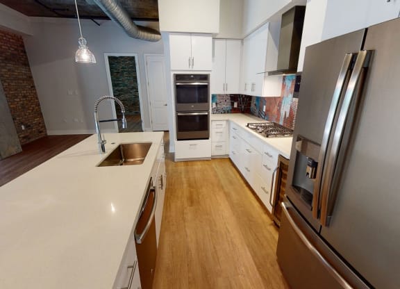 Modern kitchen here at Roosevelt Row Apartments with light wood flooring, sleek stainless steel fridge, white cabinetry, mosaic backsplash, dual ovens, and central island sink.