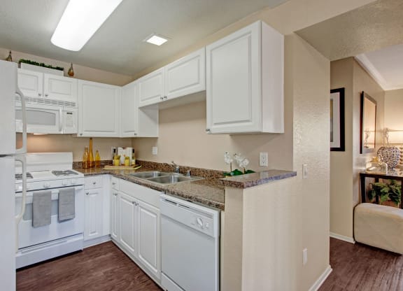 Bright kitchen here at Castlepark Apartment Homes with white cabinets, granite countertops, and stainless steel sink. Modern stove and microwave. Warm, inviting tone.