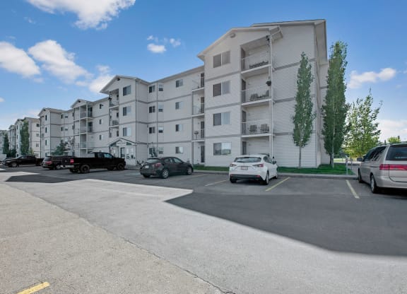 Four-story white Edgewood Estates Apartment Homes building under blue sky, with several parked cars in the foreground. Tall trees line the building, creating a calm, suburban feel.