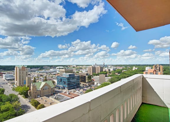 Aerial view of a cityscape from Marquis Towers Apartment Homes, featuring diverse buildings and a historic church. Fluffy clouds and a bright blue sky create a serene atmosphere.