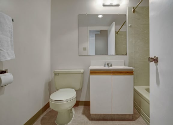 Small bathroom here at Marquis Towers Apartment Homes with clean design, featuring a beige toilet, white vanity with a mirror, and a towel on the wall. Neutral tones create a simple, tidy look.