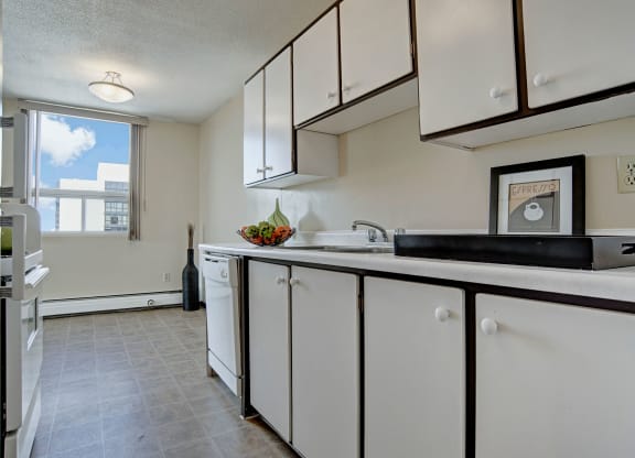 Bright kitchen here at Marquis Towers Apartment Homes with white cabinets, a large window letting in natural light, and fruit bowl on counter. Modern, clean, and minimalistic feel.