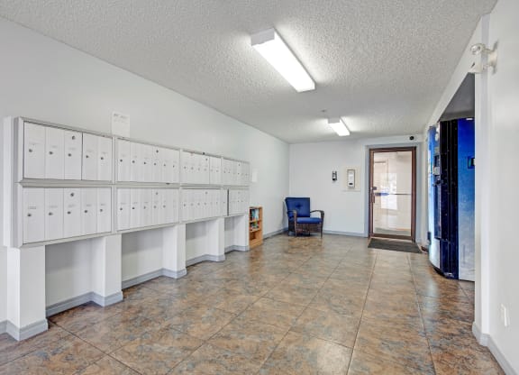 Bright, clean lobby here at Westhaven Estates Apartment Homes with white mailboxes on the left, a blue chair and small bookshelf to the right, and a vending machine near the entrance.