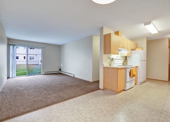 Open-plan apartment here at Westhaven Estates Apartment Homes with beige walls and mixed flooring. A sunny living area with large windows and a compact kitchen with wooden cabinets and white appliances.