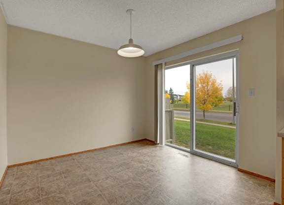 Empty room here at Westhaven Estates Apartment Homes with beige walls and a hanging light fixture. Large sliding glass doors reveal an autumn scene with a tree and grass outside.
