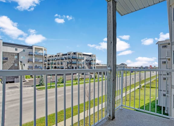 View from a balcony here at Windsor Terrace Apartment Homes showing a modern apartment complex across the street under a clear blue sky. The scene feels open and airy, with neatly trimmed grass.