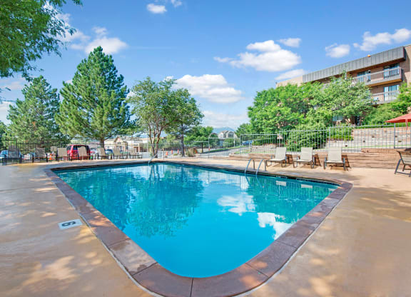 Outdoor swimming pool here at Eagle Ridge Apartment Homes surrounded by lounge chairs and trees, under a clear blue sky. The scene is peaceful and inviting, conveying relaxation.