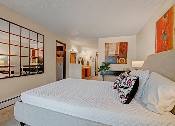 A modern bedroom here at Eagle Ridge Apartment Homes featuring a neatly made bed with floral pillows, a patterned wall mirror, abstract art, and gentle lighting, exuding a calm, stylish ambiance.