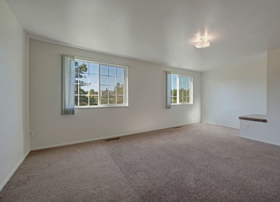 Bright, empty room here at Yorkshire Square Apartment Homes with beige carpet, white walls, and two large windows with vertical blinds. Ceiling light casts soft glow, creating a spacious feel.