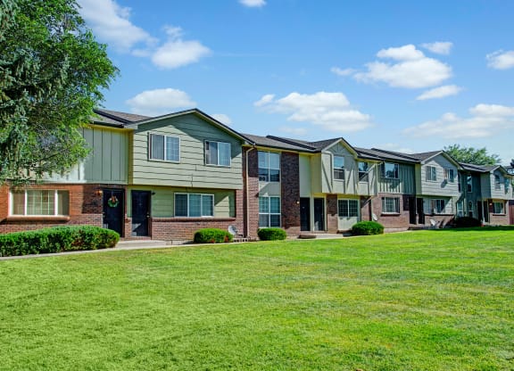 Row of two-story Yorkshire Square Apartment Homes with green and brick facades under a blue sky. Manicured lawn and trees enhance the serene suburban setting.