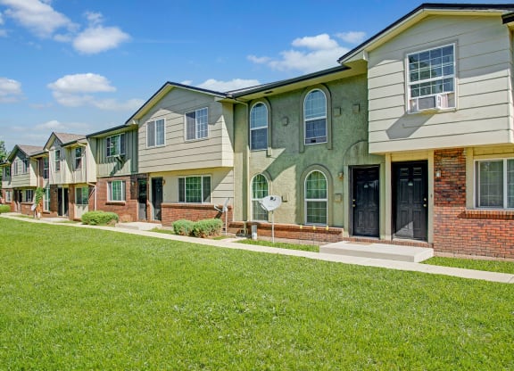 Row of modern Yorkshire Square Apartment Homes with varied facades, green lawns, and clear blue skies. The setting feels peaceful and suburban.