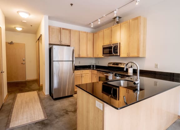 Modern kitchen here at 7west Apartment Homes with light wooden cabinets, stainless steel appliances, and a black granite countertop. It has a sleek, minimalistic design.