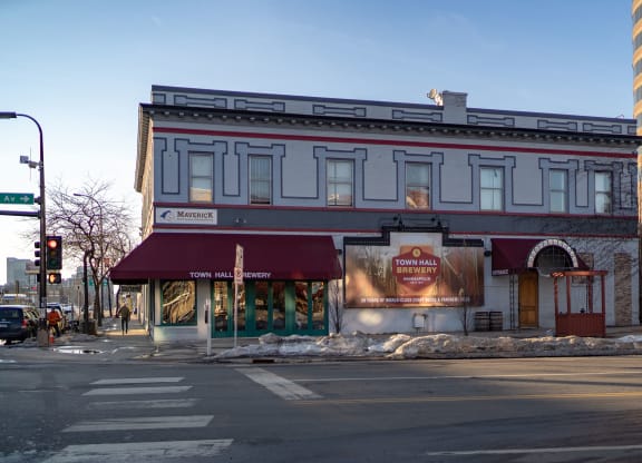 Street view of a grey, two-story building with "Town Hall Brewery" awning and sign near 7west Apartment Homes. Snow on the sidewalk, bare trees, and a clear sky.
