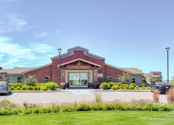 Red-brick Dakota Ridge Apartment Homes building under clear blue sky, with manicured shrubs and parked cars in front, conveying a welcoming and orderly atmosphere.