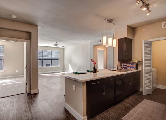 Spacious modern apartment here at the Enclave at Brookside Apartments with dark wood floors, a kitchen island, pendant lights, and a bright living area. Open door reveals an adjacent room.