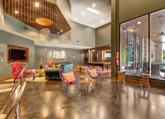 Spacious modern lounge here at the Enclave at Brookside Apartments with colorful furniture and high ceilings, featuring a pool table, wall art, and bright lighting for a lively, inviting atmosphere.