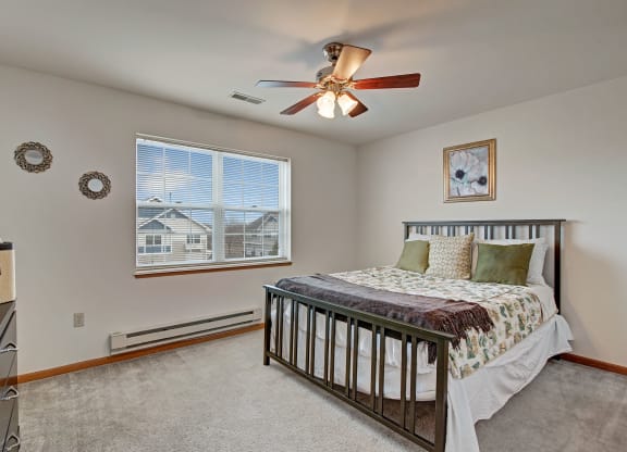 Bedroom with a metal-framed bed, floral bedding, and green pillows at Arbor Ridge Apartments. A ceiling fan, wall art, and two round mirrors enhance the cozy ambiance.