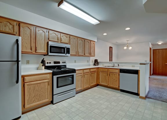 A spacious kitchen with wooden cabinets, stainless steel appliances, and tiled flooring. The room is well-lit, conveying a warm, inviting atmosphere. Arbor Ridge Apartments