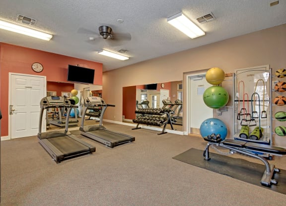 A brightly lit gym with treadmills, dumbbells, exercise balls, and resistance bands. Mirrors on the wall enhance the spacious feel at St. James Apartments.