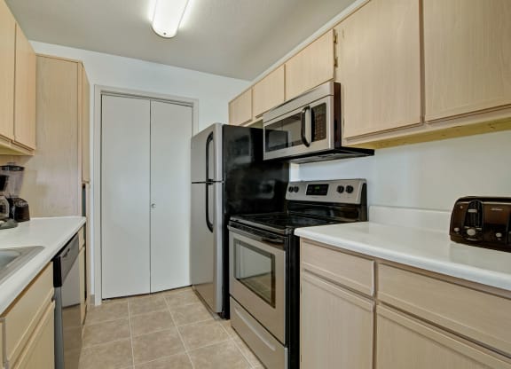 A modern kitchen with light wood cabinets, stainless steel appliances, and black accents. A coffee maker and toaster are on the counters at St. James Place Apartments.