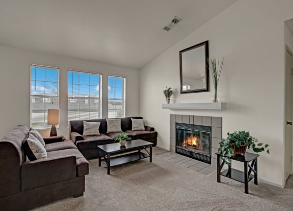 Cozy living room with brown sofas, a lit fireplace, and a mirror above the mantel. Large windows let in natural light at St. James Place Apartments.