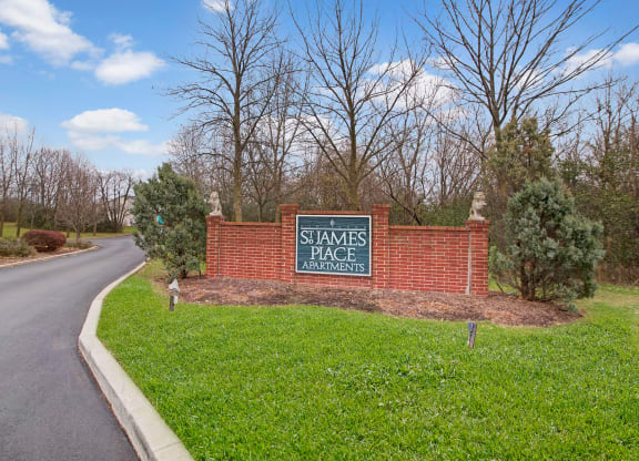 Entrance sign for St. James Place Apartments with a brick structure, surrounded by greenery and bare trees under a partly cloudy sky. Peaceful atmosphere.