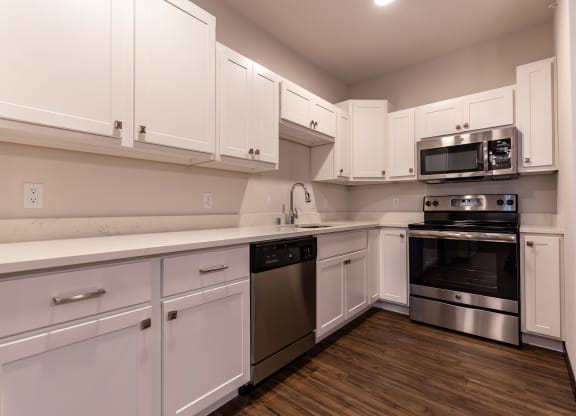 Modern kitchen at the Park Apartments with white cabinets, granite countertops, stainless steel appliances, and wood flooring. The space is clean and well-lit.