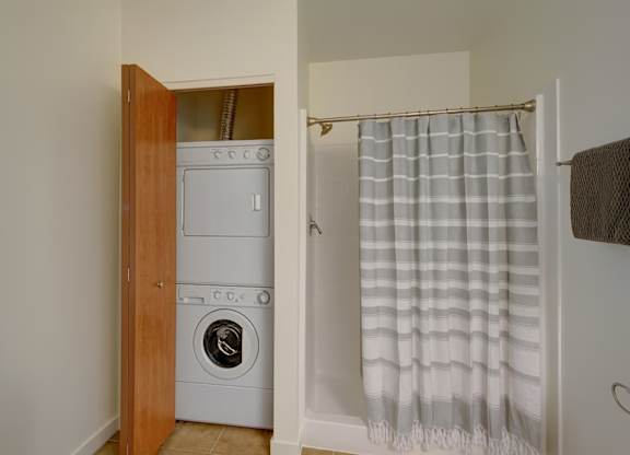 A functional bathroom here at Latitude featuring full shower and tub, convenient in-unit washer and dryer, clean finishes, and bright lighting, creating a practical and comfortable space.