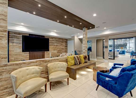 A modern clubhouse space here at River House featuring white and blue comfortable sofas, a large flatscreen tv, and bright lights giving the space an open, cozy, and welcoming feel for residents.