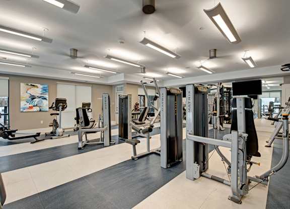 A modern fitness center here at River House including weights and strength training equipment, encompassed in an open, bright, and motivating workout envrionment.