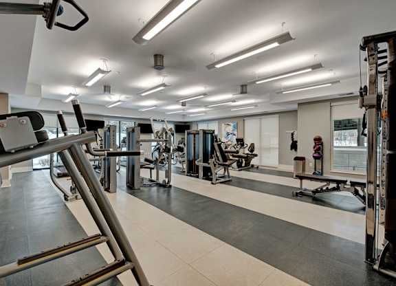 A modern fitness center here at River House including several exercise equipment, bright lights, and large windows, creating a motivating workout envrionment,