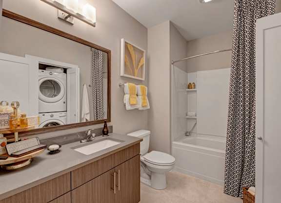 A bright and clean bathroom here at River House featuring a large wooden vanity with a large mirror and an open bathtub-shower with a black and white shower curtain, creating a fresh clean space.