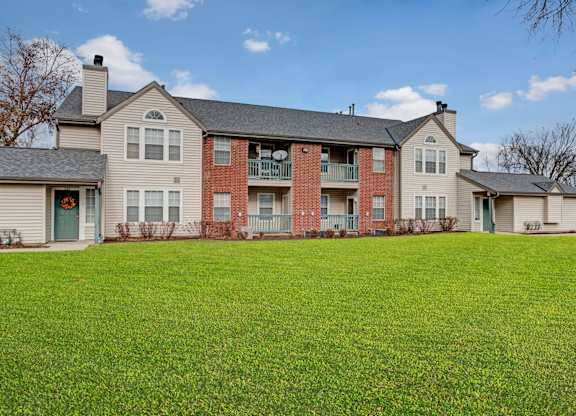A charming exterior here at St. James Place with classic brick and siding, private balconies, and large windows. A spacious green lawn and well-maintained landscaping create a peaceful and welcoming community setting.