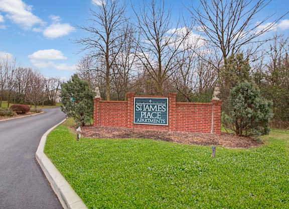 A welcoming community entrance here at St. James Place with a classic brick monument sign and landscaped greenery. A curved driveway and mature trees create a peaceful and inviting first impression.