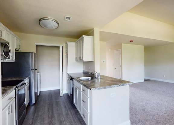 A spacious kitchen here at St. James Place with white cabinets, granite-style countertops, and stainless steel appliances. A breakfast bar overlooks the open living area, creating a bright and inviting layout.
