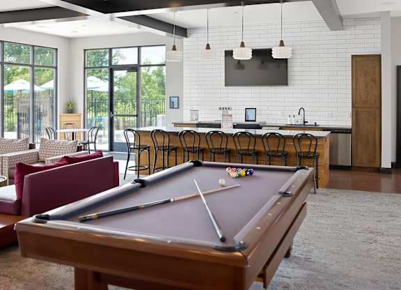 A pool table is in the middle of a room with a bar and a television.