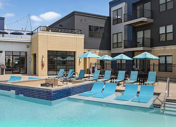 A pool with blue chairs and umbrellas in front of a building.