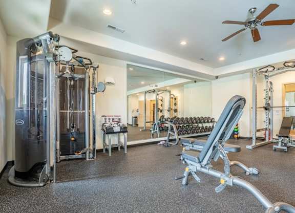 A modern fitness center here at Van Buren Place with strength machines, free weights, and an adjustable bench. A mirrored wall enhances the spacious feel, while bright lighting and rubber flooring create a clean, energizing atmosphere.