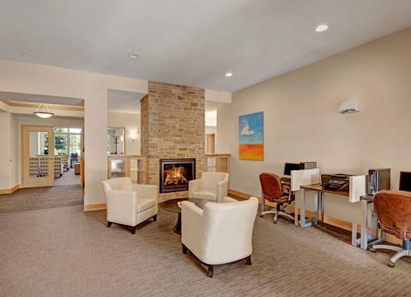 A welcoming resident lounge here at Van Buren Place with comfortable seating arranged around a cozy stone fireplace. A business center with computers and desks provides convenience, while warm lighting and soft carpeting create a relaxed, inviting atmosphere.