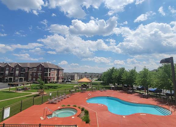 A scenic outdoor pool here at Van Buren Place with a relaxing spa and spacious sundeck. A shaded gazebo, comfortable lounge seating, and surrounding green landscaping create a bright, resort-style atmosphere.