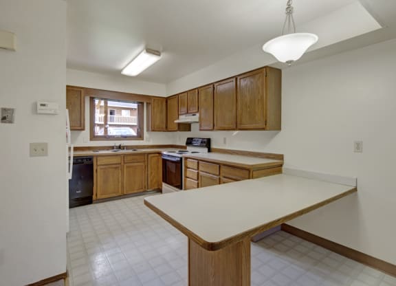 Spacious kitchen here at Wildwood Estates Apartments with wooden cabinets, white countertops, and an island. Bright natural light from window, creating an inviting and clean atmosphere.