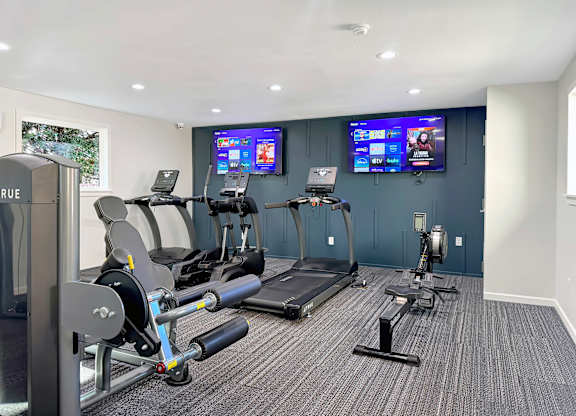 a gym with exercise machines and two televisions on the wall