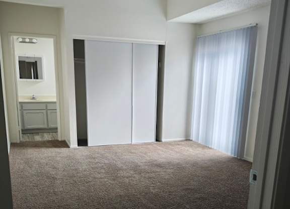 A carpeted room with a white door and a window with curtains.