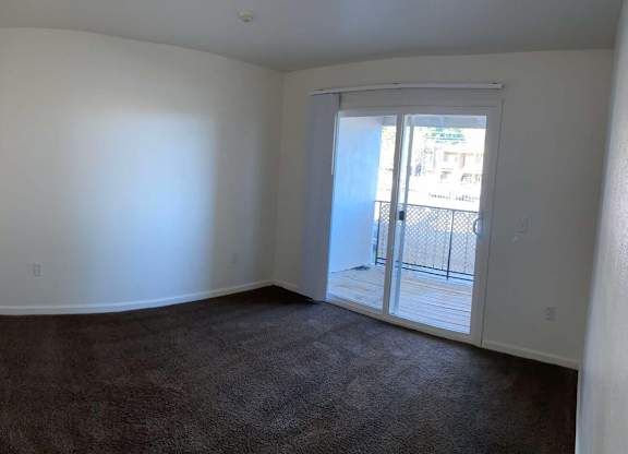 A room with a carpeted floor and a sliding glass door leading outside.
