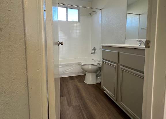 A white toilet sits in a small bathroom with wood floors and white walls.