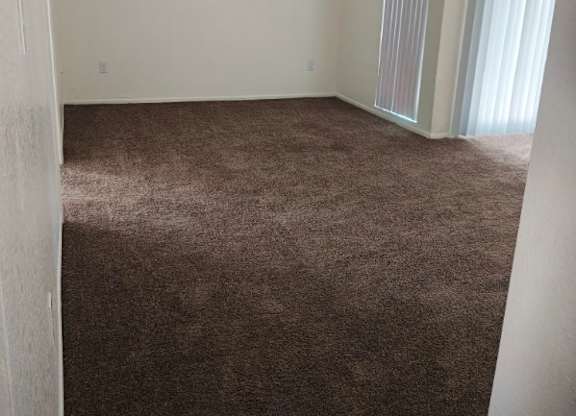 A room with a carpeted floor and a window with curtains.