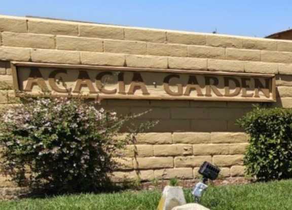 A sign that says "Acacia Garden" is mounted on a tan wall.