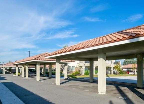 A parking lot with a series of white pillars supporting a red tile roof.